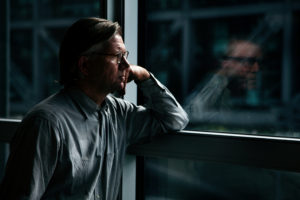 Man stands near window, looking at his reflection