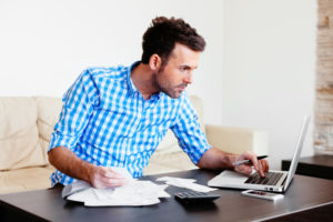 A man works on his finances while kneeling in front of his living room table.