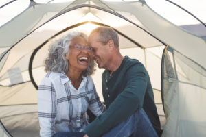 A man whispers to his laughing wife inside a cozy tent.