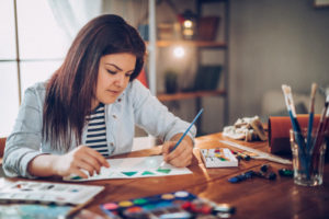 Teen sits at table, painting