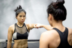 A woman in gym clothes touches her fist to her reflection.