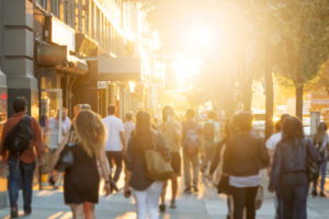 Crowd of people walking on busy sidewalk and carrying shopping bags