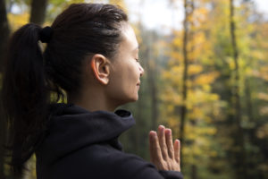 Woman standing in forest with hands together, meditating