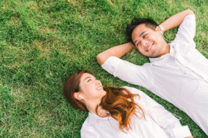 A young couple wearing white shirts lie side by side on spring grass.