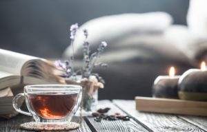 A cup of herbal tea next to some candles and lavender flowers