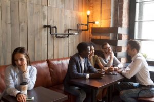 Group of friends sit in cafe, ostracizing one person from their social group