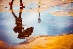 Reflection of woman walking with an umbrella in a puddle