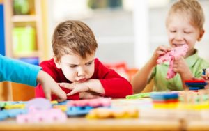 Angry boy sits at table, looking at a puzzle.