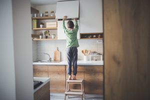 Young boy standing on step stool to steal cookies form kitchen cupboard