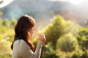 Woman standing outside, looking thoughtful while she holds a coffee cup.