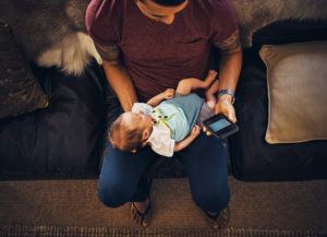 A father holding his newborn is distracted by his phone