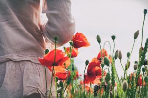 Side view of woman standing in field of tall red poppies