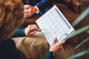 Therapist marking a date on a cluttered calendar with client in the background