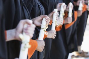 Closeup on the hands of a line of graduates who are holding their diplomas