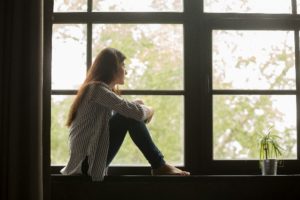 Girl sitting on windowsill, looking outside at some trees.