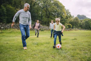 Three men and a young boy play soccer on an empty field.