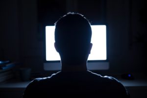 Silhouette of man sitting in front of a computer in the dark