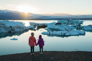 Sisters hold hands and watch a melting glacier.
