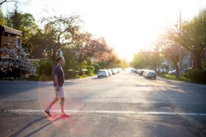 Man walking across street in a quiet neighborhood at sunset