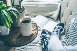 View of someone's feet in cozy socks with a book and coffee on a couch
