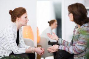 Woman sitting next to mirror that reflects her while speaking with a therapist