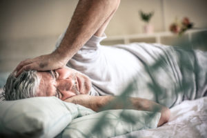 Senior man lying on bed and having migraine.