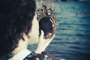 Woman looking into ornate, hand-help mirror
