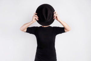 Woman holding up a black hat to hide her face