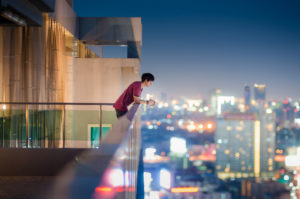 Man in red shirt leans on railing to look at city