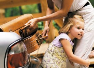 Child hugging parent as they pack suitcases into car for a trip