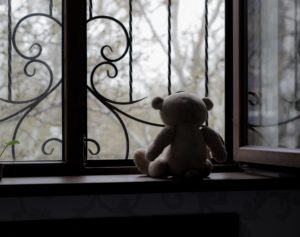 Sad child's teddy bear in the window.