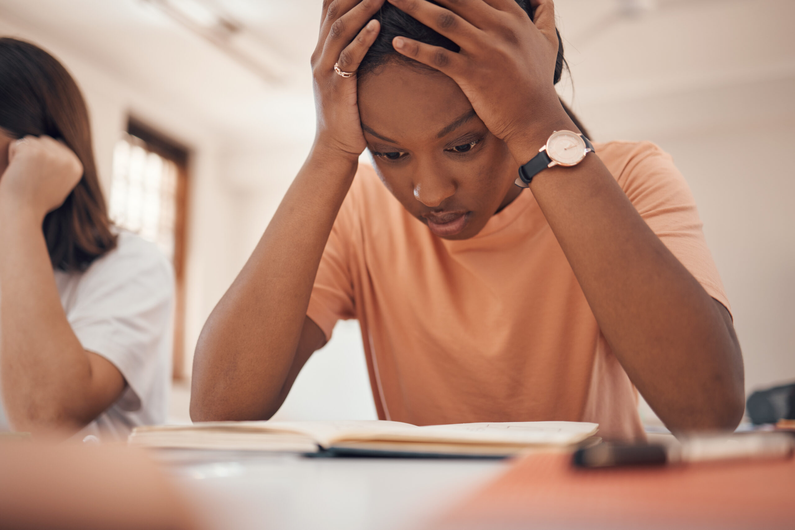 Young girl with hands on her head reading a book stressed