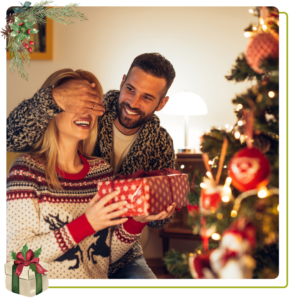 casal dando um para um ao outro um presente ao lado da árvore de Natal