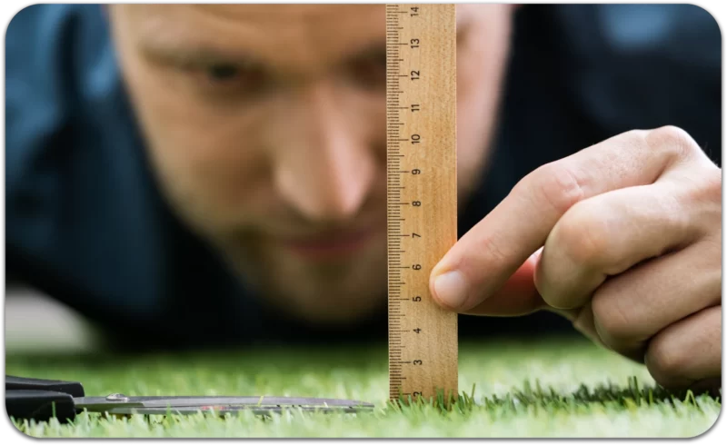 Man measuring individual blades of grass with a ruler, symbolizing Perfectionism and Childhood Trauma.