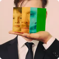 A man in a suit holds a glass prism showing his face split into childhood, adult, and reflective layers, symbolizing impostor syndrome and identity conflict.