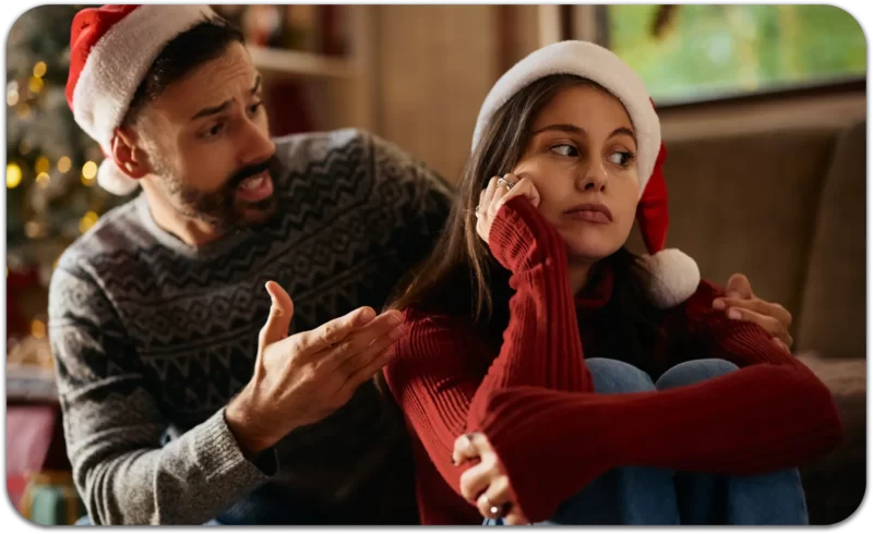 4 Ways to Navigate Holiday Family Conflict: Finding the Quite Middle 2 Couple in Santa hats arguing on the couch during holiday family conflict