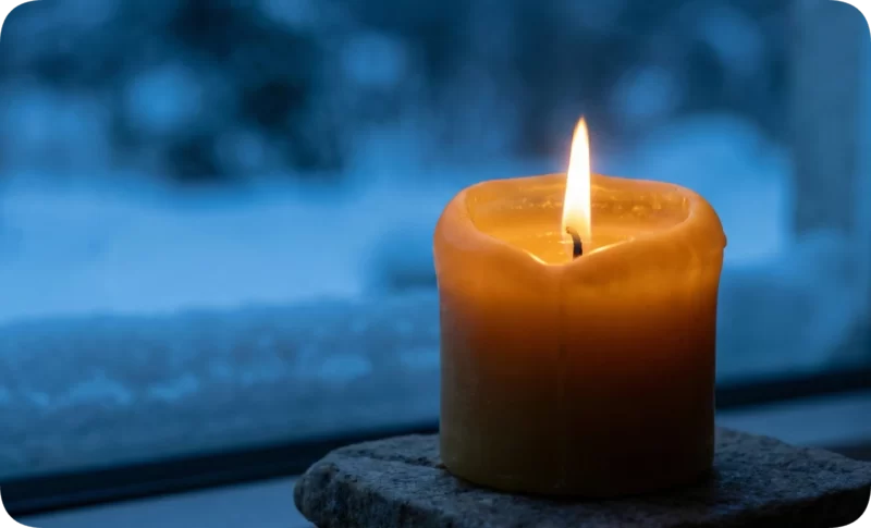 The Loneliest Time of the Year? Here’s How to Survive SAD 3 Warm glowing candle on a stone slab against a blurry blue winter window, symbolizing comfort against seasonal affective disorder.