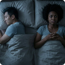 A young woman lies awake in bed, hands clasped, grappling with self-doubt in relationships and nighttime anxiety.