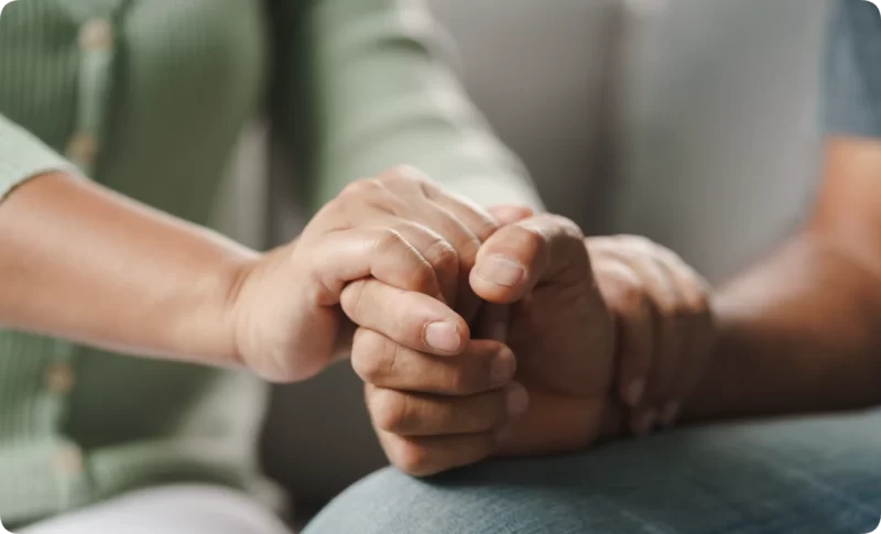 Close-up of a therapist gently holding a client's clasped hands during a supportive types of therapy session, showing empathy and connection