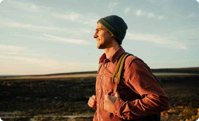 A young man with a backpack smiling outdoors, symbolizing finding closure and moving forward with hope