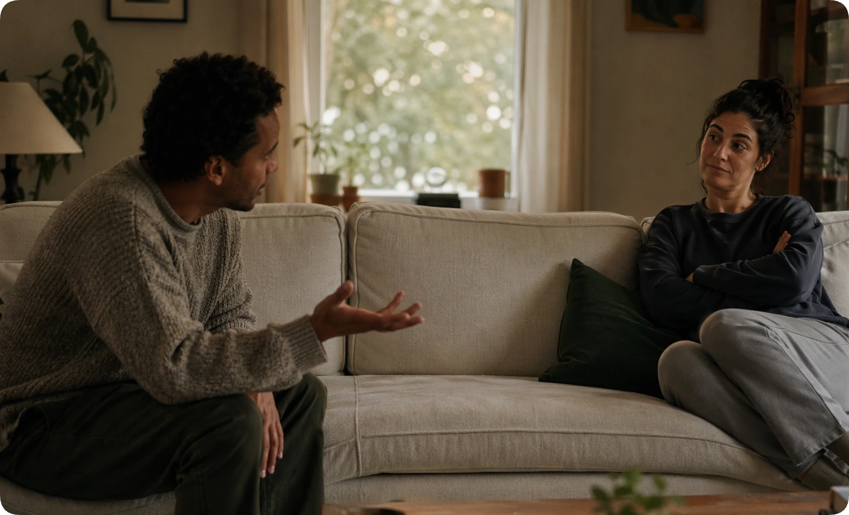 A couple sitting apart on a couch with one partner dismissive and the other explaining, depicting the power imbalance of gaslighting in relationships