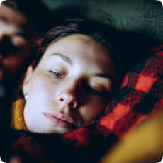 Young woman resting peacefully with eyes closed, wrapped in a red plaid blanket, finding relief from news anxiety and doomscrolling