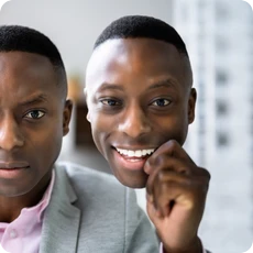 A professional holds a smiling mask beside his unsmiling face, showing the feeling of imposter syndrome.