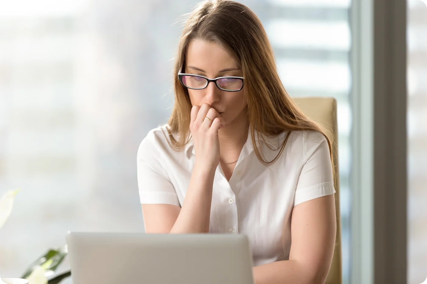 A professional looks uncertain while working at a laptop, reflecting self-doubt associated with imposter syndrome.
