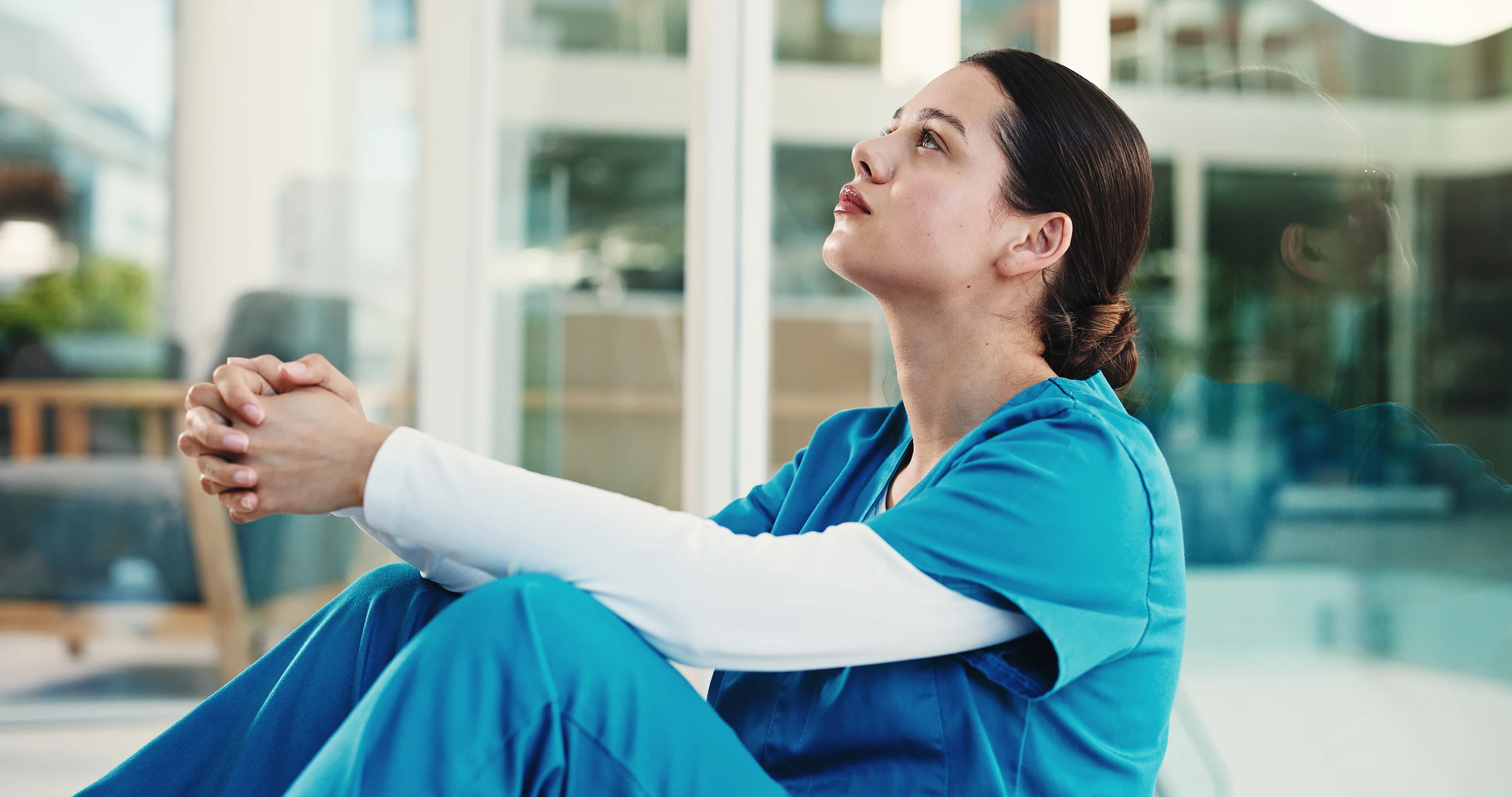 A healthcare worker sitting quietly by a window, reflecting workplace grief after a stressful job