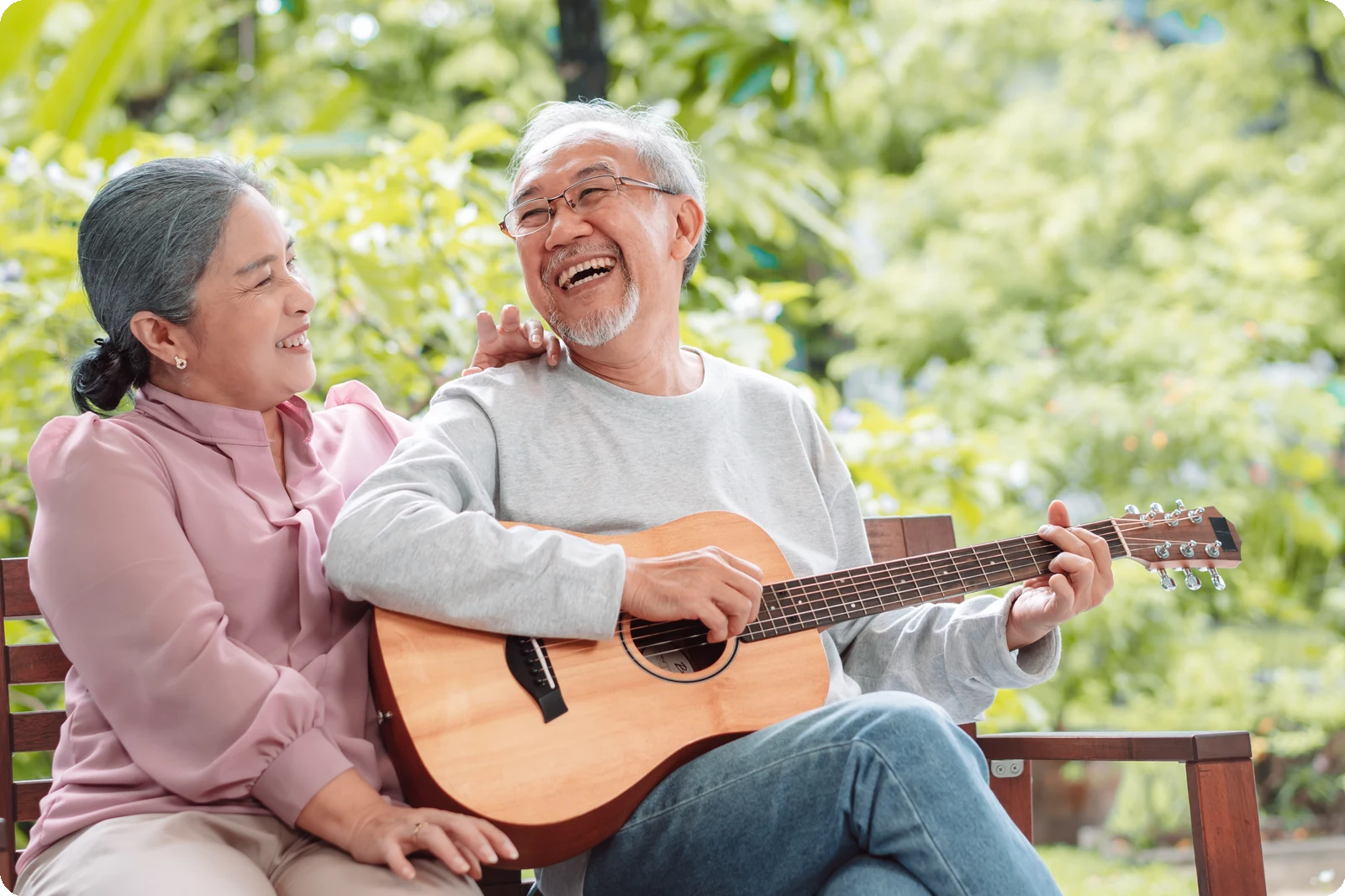Older couple smiling together on a garden bench while one plays guitar, reflecting senior years mental health, joy, and connection.