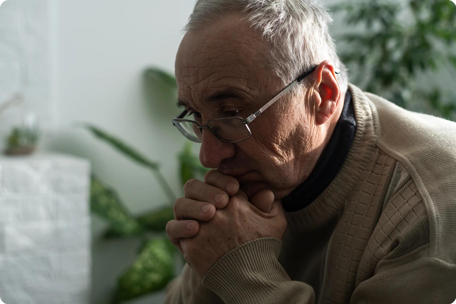 Older man sitting in quiet reflection with hands folded, representing senior years mental health, prayer, stress, and life review.