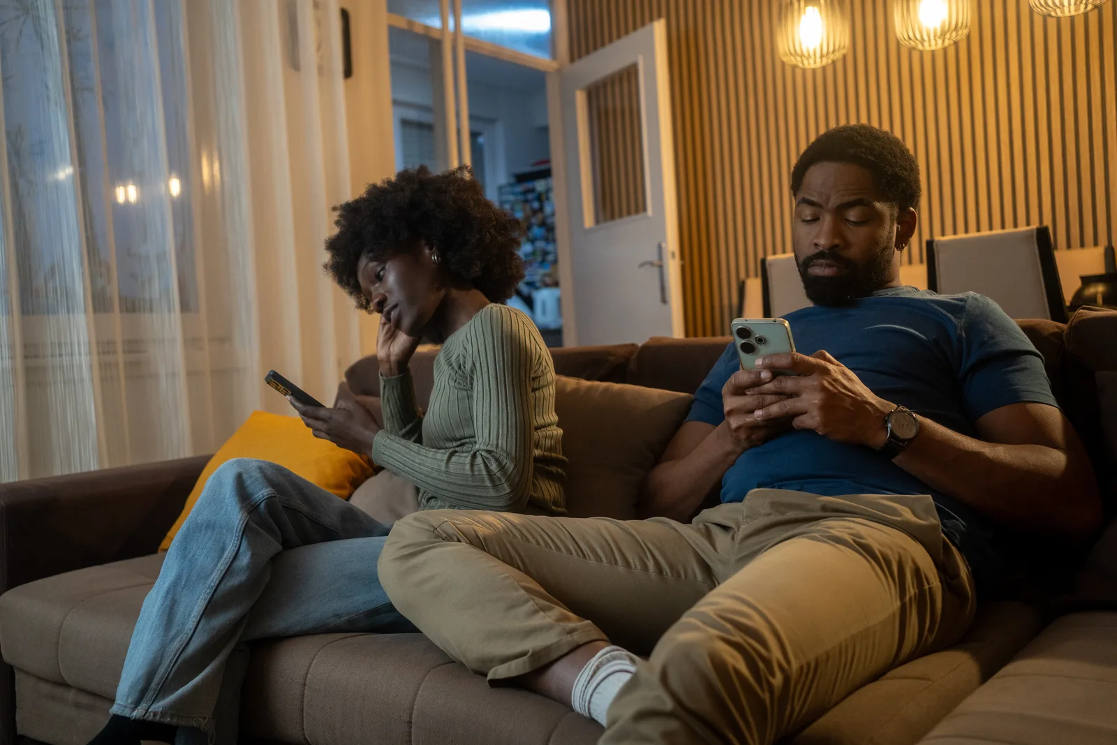 A couple sits quietly after a tense conversation, each holding a phone.