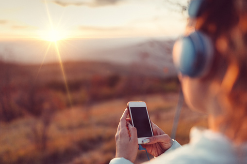 Woman standing in field at sunrise listening to podcast with headphones.