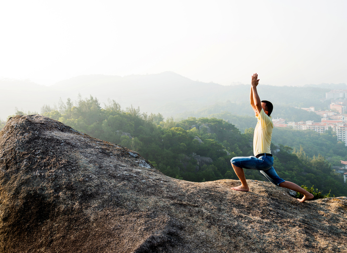 Man in yoga pose on rock ledge